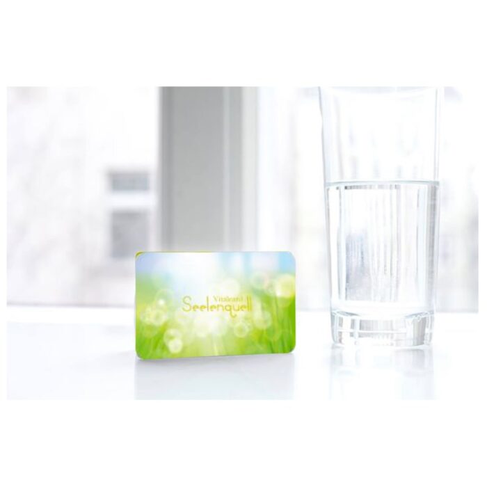 A glass of water placed on the Raumvital "Seelenquell" Vitalcard, with a subtle glow, suggesting spiritual clarity.